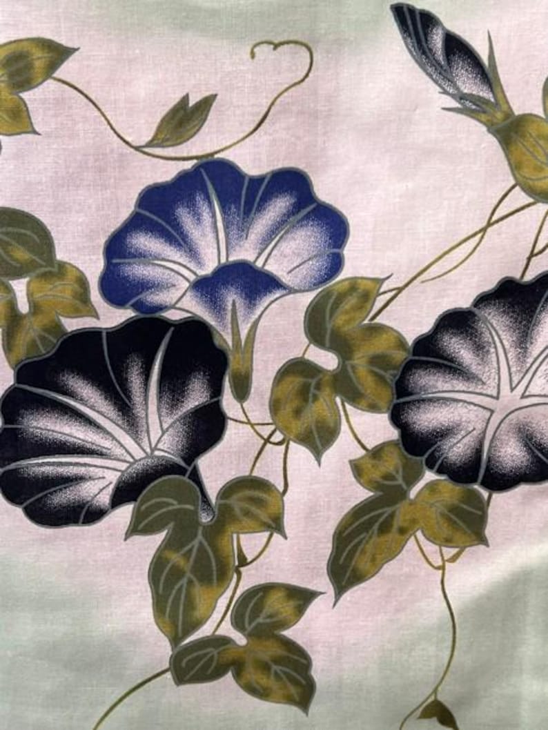 Op de afbeelding: Een stof met een botanische print van ochtendgloriebloemen in tinten diepblauw, paars en wit, vergezeld door olijfgroene bladeren en dunne, kronkelende wijnstokken op een bleke, lichtgekleurde achtergrond met een subtiel kleurverloop.