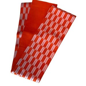 May include: A long, rectangular obi sash featuring a vibrant orange base color. The fabric is decorated with a repeating pattern of white, stylized arrow feathers arranged in vertical columns across the entire length of the textile accessory.
