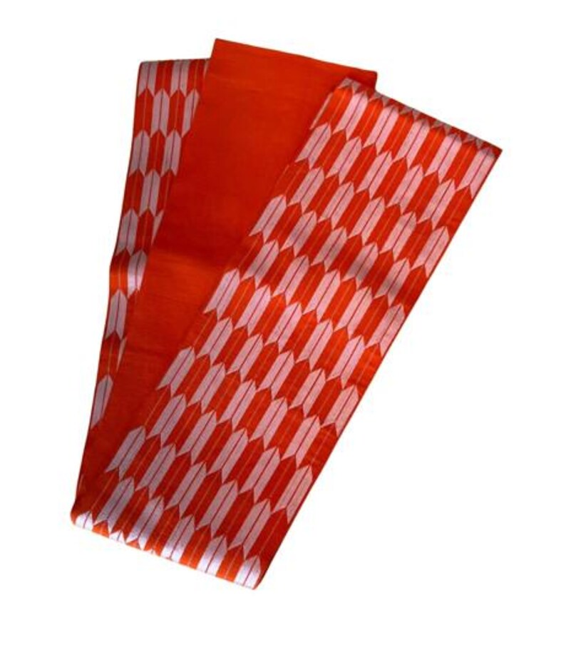 May include: A long, rectangular obi sash featuring a vibrant orange base color. The fabric is decorated with a repeating pattern of white, stylized arrow feathers arranged in vertical columns across the entire length of the textile accessory.