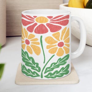 May include: White ceramic mug with a floral design. The flowers are red, yellow, and green. The mug has a handle.