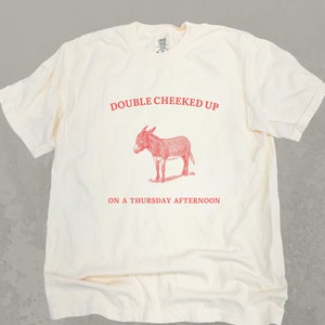 May include: A white t-shirt with a red graphic of a donkey and the text "Double Cheeked Up On A Thursday Afternoon".