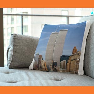 May include: A decorative pillow featuring an image of the Twin Towers in New York City against a blue sky. The pillow showcases the iconic skyscrapers amidst a cityscape of other buildings.