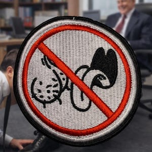 May include: Embroidered patch with a black and white graphic of a cartoon penis crossed out with a red line. The patch is circular with a black border and a light gray background. The patch is on a gray surface.