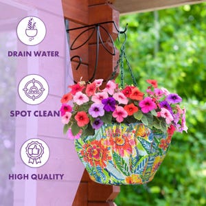 May include: A colorful hanging planter with a floral pattern. The planter is filled with pink, purple, and red flowers. The planter is hanging from a black metal hook.