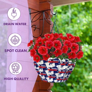 May include: A white hanging planter with a blue and red buffalo print. The planter is filled with red petunias and is hanging from a black metal hook.