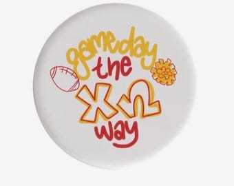 May include: White circular button with the text "gameday the X way" in yellow and red. Includes a football and a pom-pom graphic. Perfect for game day.