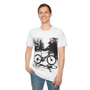 May include: White t-shirt with a black and white graphic of a bicycle in a forest setting. The graphic includes a red circle in the upper right corner.