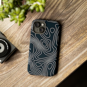 Może przedstawiać: Czarne etui na telefon z białym wzorem topograficznej mapy. Etui ma wystający element z dwoma obiektywami aparatu.