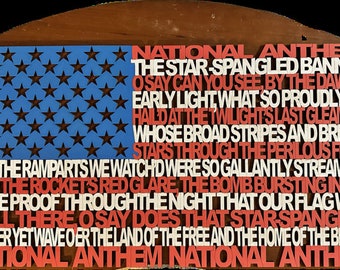 Puede incluir: Un letrero de madera con forma de bandera con las palabras "National Anthem" y la letra de "The Star-Spangled Banner" impresas en letras rojas, blancas y azules. El letrero tiene un fondo azul con estrellas blancas.