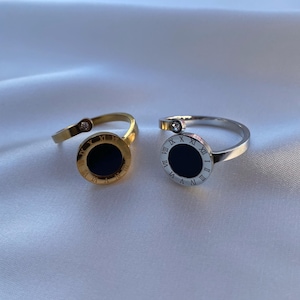 May include: Two gold and silver rings with black face and Roman numeral markings. The rings are on a white fabric background.