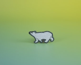 Può includere: Toppa ricamata con un orso polare bianco con contorno grigio, che cammina verso destra. La toppa è posta su uno sfondo sfumato verde e giallo.