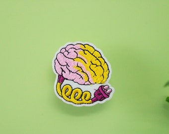 May include: An embroidered brain patch in pink and yellow with a purple and yellow cord and plug. The brain is connected to the plug by a yellow cord that is coiled.