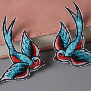 Peut inclure: Deux patchs brodés thermocollants représentant des hirondelles bleues et rouges. Les hirondelles sont tournées dans des directions opposées.