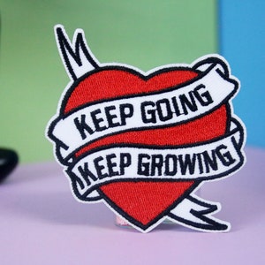 May include: Red embroidered heart with white banner and black text that reads "Keep Going Keep Growing".