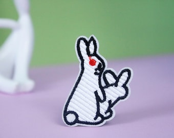 May include: White embroidered iron-on patch of a rabbit giving the middle finger. The rabbit has a red eye.