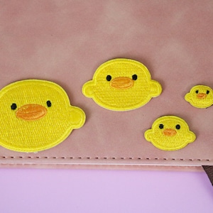 May include: Four yellow felt duck patches of varying sizes, sewn onto a pink notebook cover.