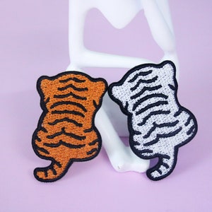 May include: Two embroidered iron-on patches of tigers. One tiger is orange and black, the other is white and black.