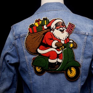 May include: A light blue denim jacket with a large embroidered patch of Santa Claus on a green scooter. Santa is in a red suit, carrying a sack of gifts. The patch includes the text "HO HO HO".