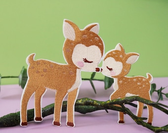 以下が含まれることがあります： 白い斑点のある茶色の鹿の刺繍アイロン接着パッチ2枚。1つは大きく、もう1つは小さく、大きな鹿が小さな鹿の頭をキスしている。