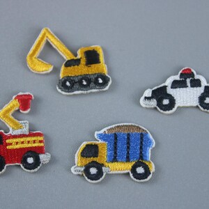 May include: Four embroidered iron-on patches featuring different vehicles: a yellow excavator, a red fire truck, a blue dump truck, and a white police car.