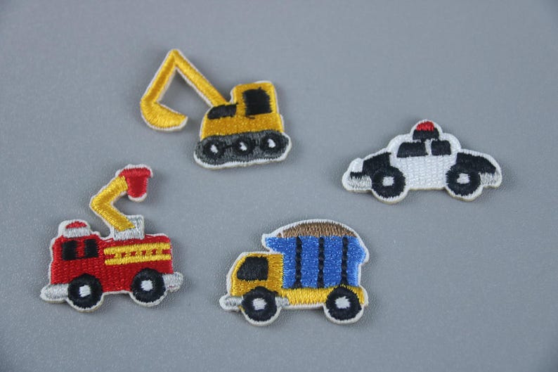 May include: Four embroidered iron-on patches featuring different vehicles: a yellow excavator, a red fire truck, a blue dump truck, and a white police car.