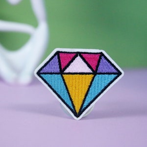 May include: A colorful diamond-shaped embroidered patch with pink, purple, blue, and yellow geometric shapes.