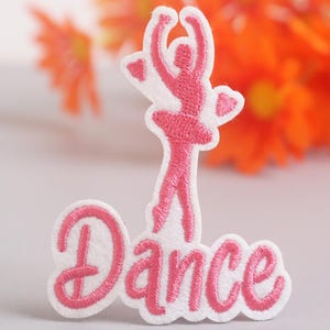 Op de afbeelding: Geborduurde patch met een roze ballerina silhouet en het woord "Dance" in cursief. De patch heeft een witte rand. De achtergrond is wazig, met oranje bloemen. Geschikt voor kleding.