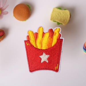 May include: Red and white embroidered patch of a box of french fries. The fries are yellow and orange. There is a white star on the box.