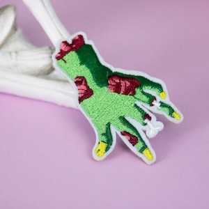 May include: Green and red embroidered zombie hand patch with yellow fingernails.