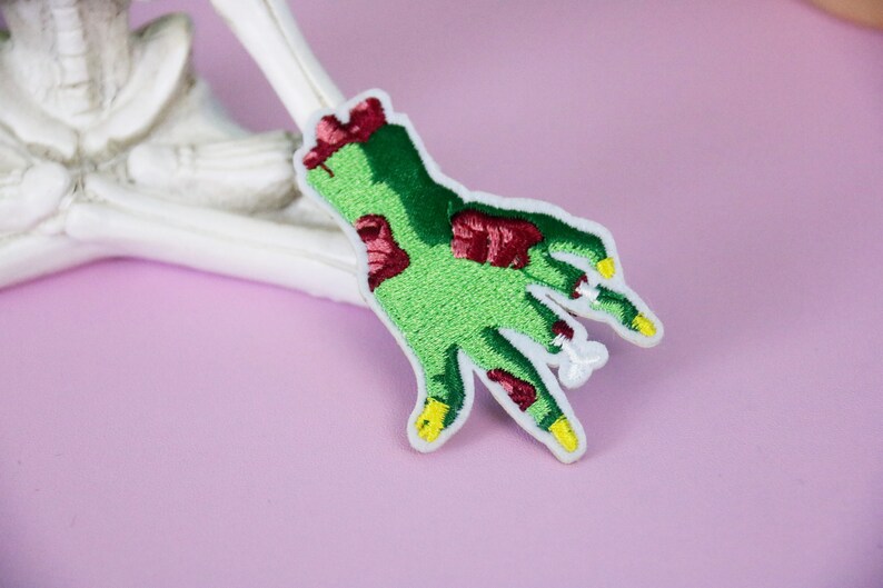 May include: Green and red embroidered zombie hand patch with yellow fingernails.