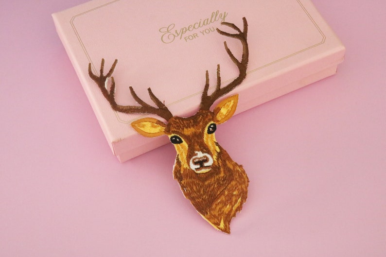 May include: A brown deer head with antlers, set against a pink background and a pink gift box. The deer has detailed features and is the focal point. The gift box has the words "Especially for You".