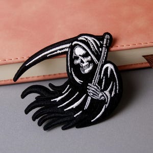 Pode incluir: Patch de ferro bordado em preto e branco da Morte segurando uma foice.
