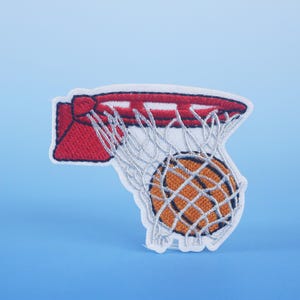 May include: A white embroidered patch of a basketball going through a red hoop with a white net.