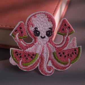 Può includere: Una toppa ricamata raffigurante un polpo rosa chiaro con grandi occhi neri e ciglia. Il polpo tiene in mano tre fette di anguria, ognuna con polpa rosa, semi neri e buccia verde, il tutto contornato da un filo di colore bianco.