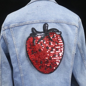 May include: A blue denim jacket with a red and black sequined strawberry patch on the back.