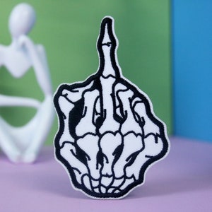 May include: Black and white embroidered patch of a skeleton hand giving the middle finger.