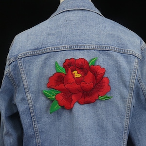 May include: A blue denim jacket with a red embroidered flower on the back.