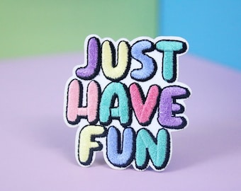 Könnte beinhalten: Ein bunter gestickter Aufnäher mit dem Text "JUST HAVE FUN" in Blasenbuchstaben. Die Buchstaben sind in verschiedenen Pastellfarben, darunter Rosa, Blau, Grün und Gelb.
