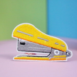 May include: Yellow and gray embroidered iron-on patch of a stapler.