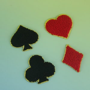 Peut inclure: Quatre symboles de jeu de cartes : un pique noir, un cœur rouge, un trèfle noir et un carreau rouge. Chaque symbole a une bordure dorée. Les symboles sont disposés sur un fond dégradé bleu clair et vert.