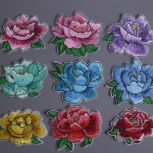 May include: Nine embroidered peony flower patches in various colours, including pink, purple, blue, and yellow, with green leaves. The patches are arranged on a grey background.
