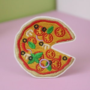 Könnte beinhalten: Ein gestickter Bügelaufkleber in Form eines Pizzastücks mit roten, gelben, grünen und schwarzen Belägen.