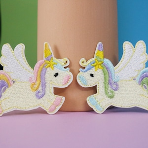 May include: Two embroidered iron-on patches of white unicorns with rainbow manes and tails, and white wings. The unicorns are facing each other.