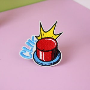 May include: A red button with a yellow crown on top and the word "CLIK" in blue letters. The button is surrounded by a blue ring.
