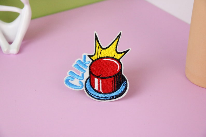 May include: A red button with a yellow crown on top and the word "CLIK" in blue letters. The button is surrounded by a blue ring.