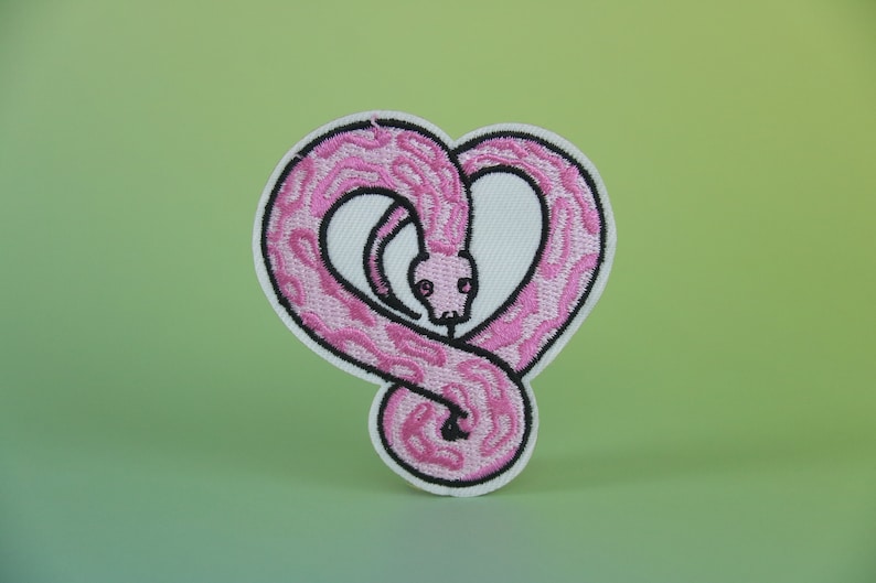 Op de afbeelding: Roze geborduurde strijkpatch van een slang die in de vorm van een hart is opgerold.