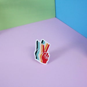 Pu&ograve; includere: Toppa ricamata colorata a forma di mano che fa il segno della pace. La mano &egrave; rossa con dita nei toni dell'arancione, giallo, verde acqua e nero. La toppa ha il testo "766" sulla mano rossa.