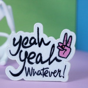 May include: White embroidered patch with black text that reads "yeah yeah whatever!" and a pink peace sign with a black eye.