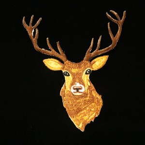 May include: Embroidered patch featuring a deer head with large antlers. The deer has a brown coat, yellow ears, and a white nose, set against a black background. This patch is suitable for apparel and accessories.