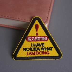 Può includere: Toppa di avvertimento gialla ricamata a forma triangolare con bordo nero. La toppa presenta la parola "WARNING" in un ovale rosso e il testo "I HAVE NO IDEA WHAT I AM DOING" in rosso e nero.